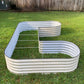 Image of the pearl white U-shaped metal raised garden bed sitting empty on the grass in a backyard. 
