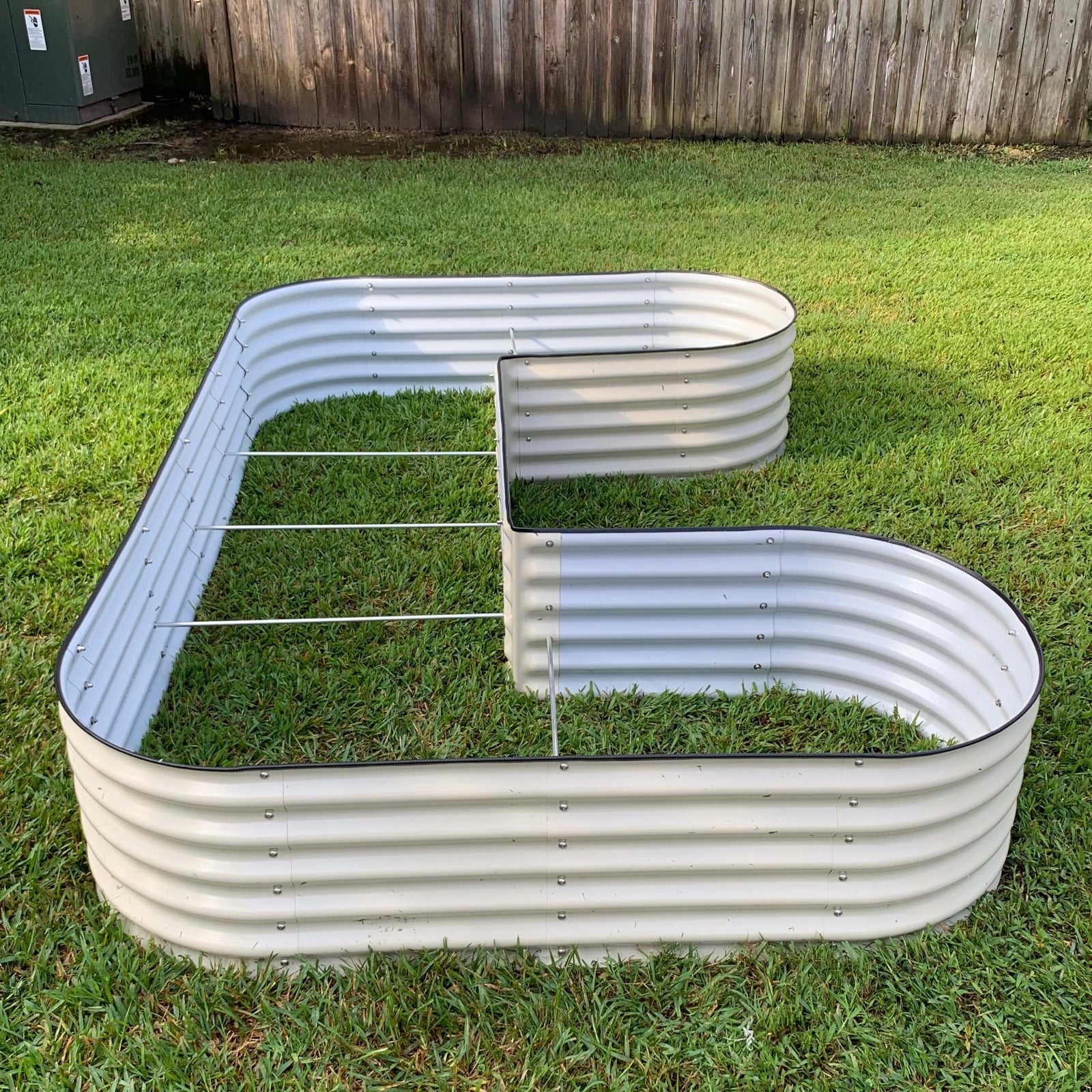 Image of the pearl white U-shaped metal raised garden bed sitting empty on the grass in a backyard. 