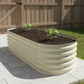 A pearl white self-watering raised garden bed with pepper plants in fenced backyard sitting on concrete pavers.
