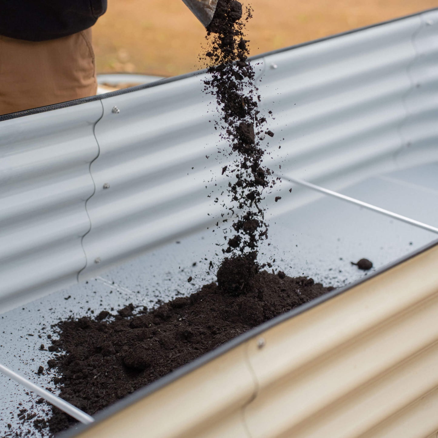 Person pouring soil into a 32 inch tall raised metal garden bed with the soil saving floor installed. 